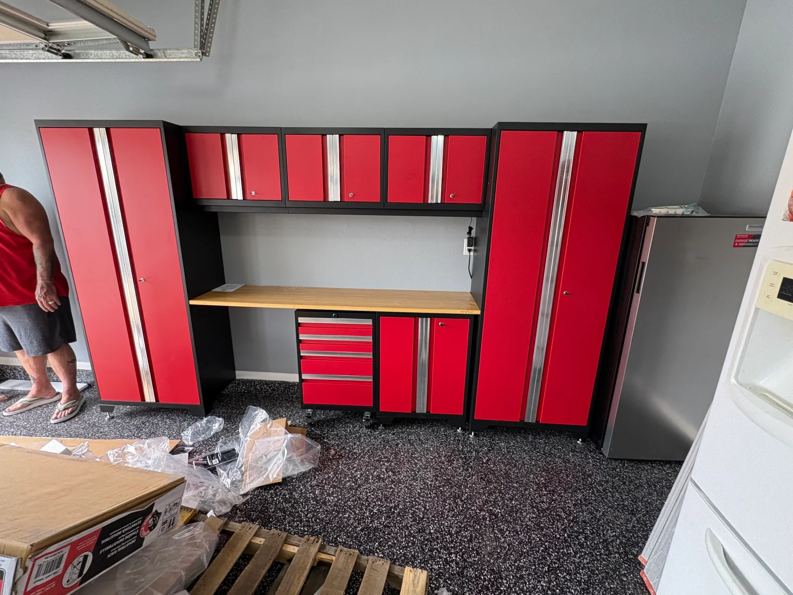Red steel garage cabinets with stainless handles, black frames, and a wood countertop workbench installed against gray wall