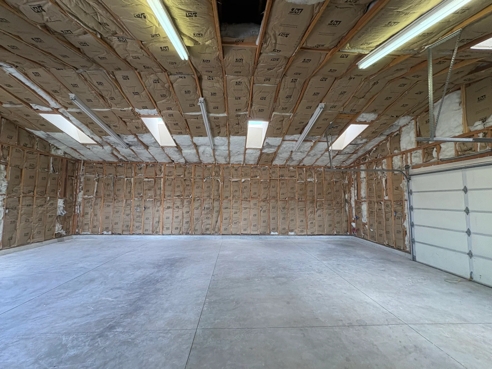 Garage interior with kraft-faced fiberglass batt insulation between exposed wood framing on walls and ceiling, concrete floor