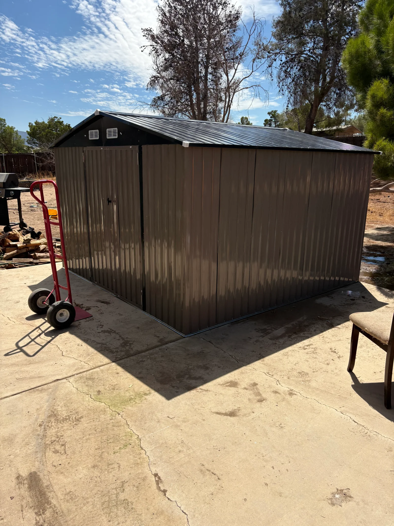 Brown corrugated metal storage shed with black roof and trim on a concrete pad, with double doors and gable vents