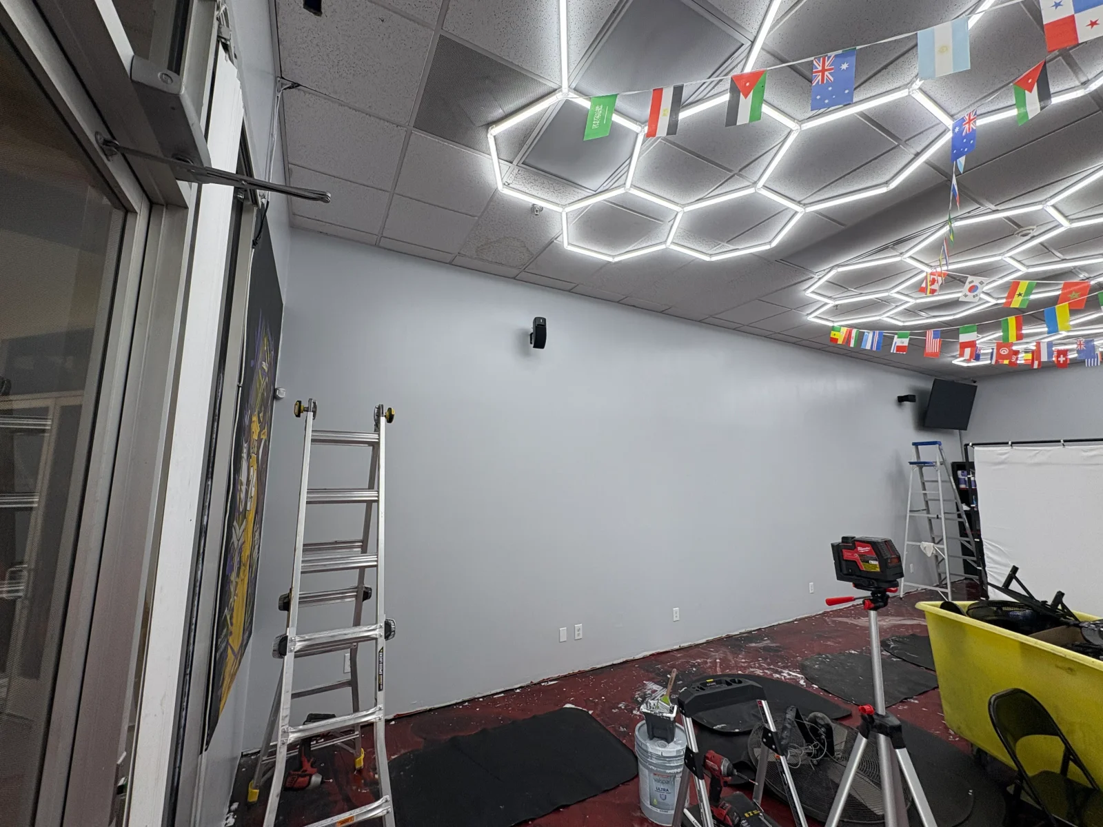 Commercial room with hexagonal LED ceiling lights, drop ceiling tiles, painted gray wall, and aluminum ladders during renovation