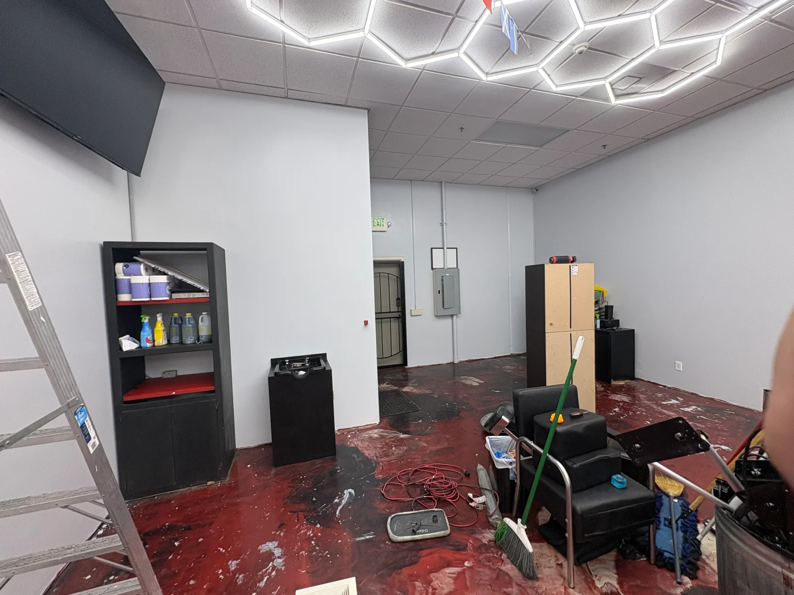Empty commercial interior with gray painted walls, hexagonal LED ceiling lights, and a red stained concrete floor during cleanup