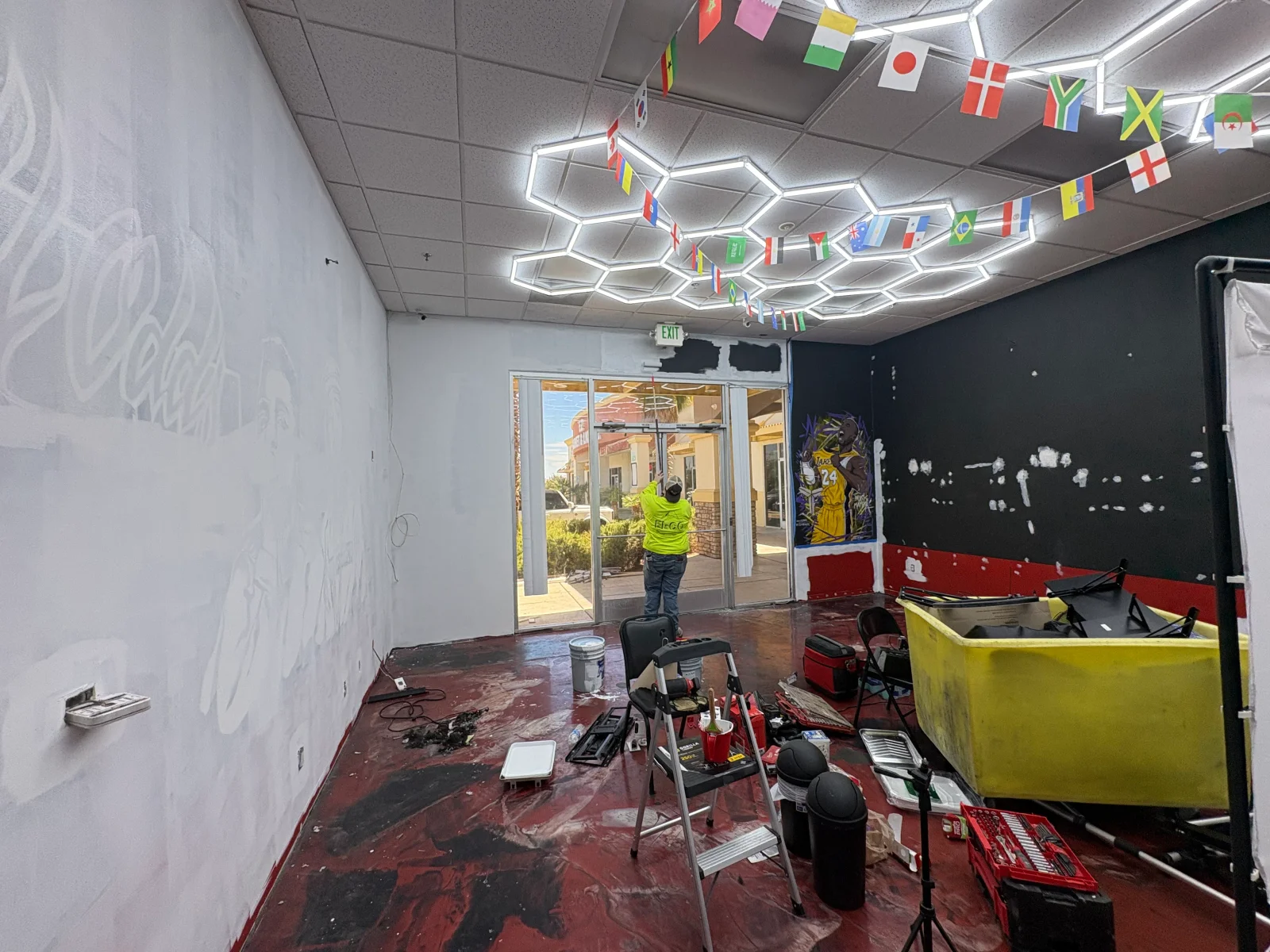 Painter on step ladder working on black accent wall with red painted base, white primed wall, and hexagonal LED ceiling lights