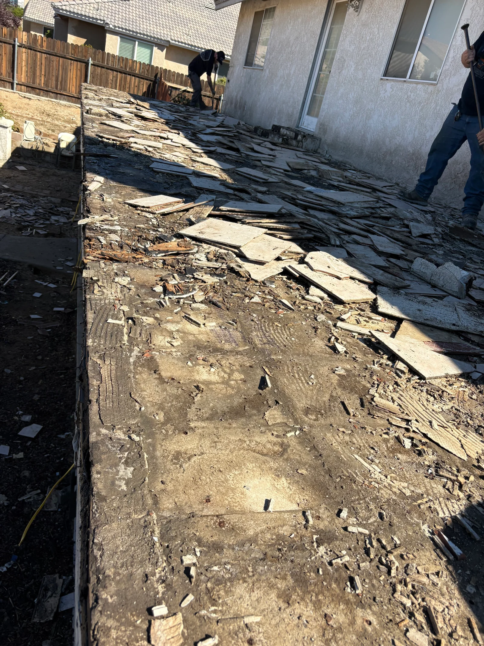 Stripped flat roof deck with broken tile, debris, and exposed sheathing during tear-off