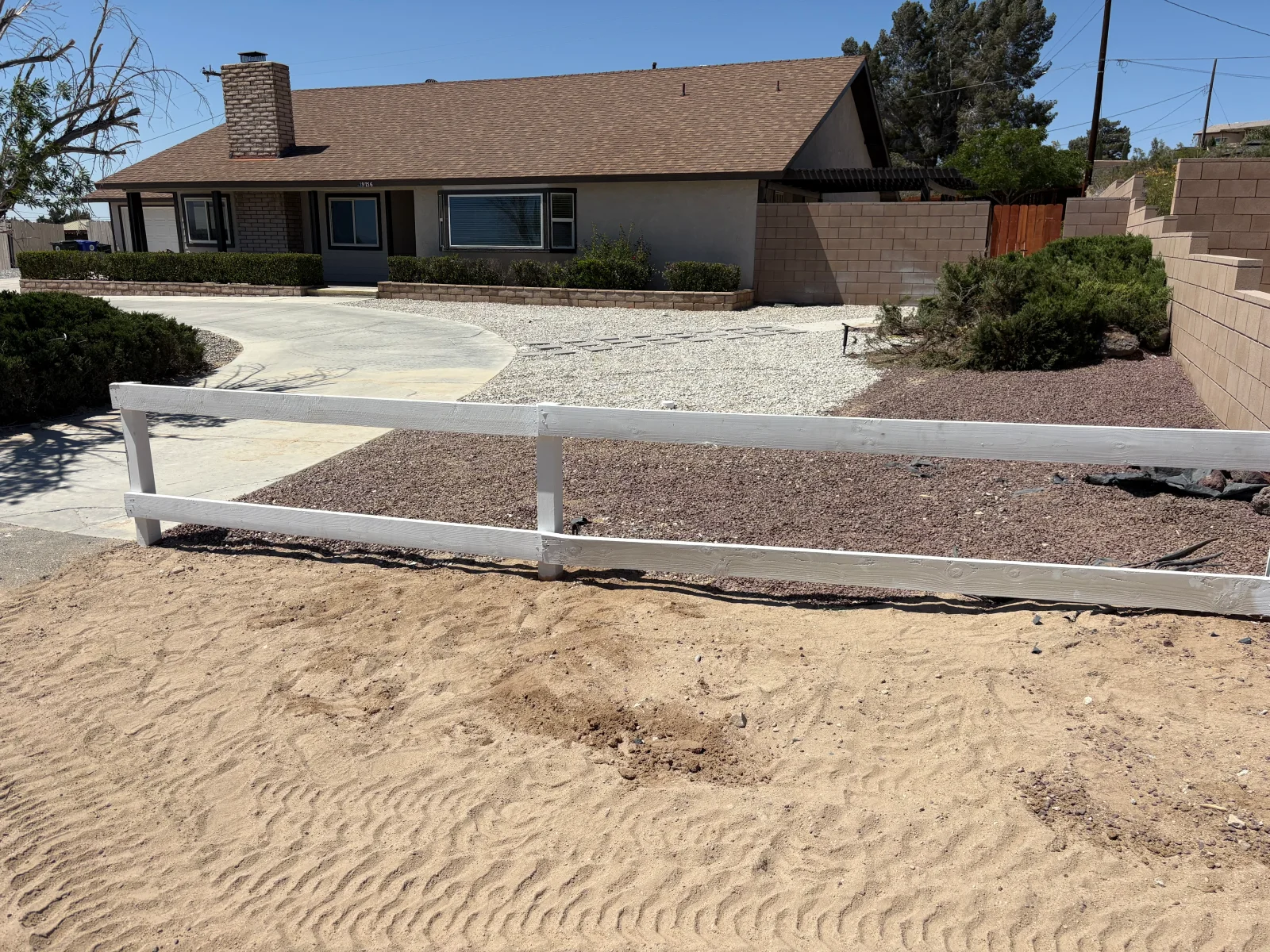 White painted two-rail wood fence with square posts beside gravel and rock mulch landscaping and a concrete driveway