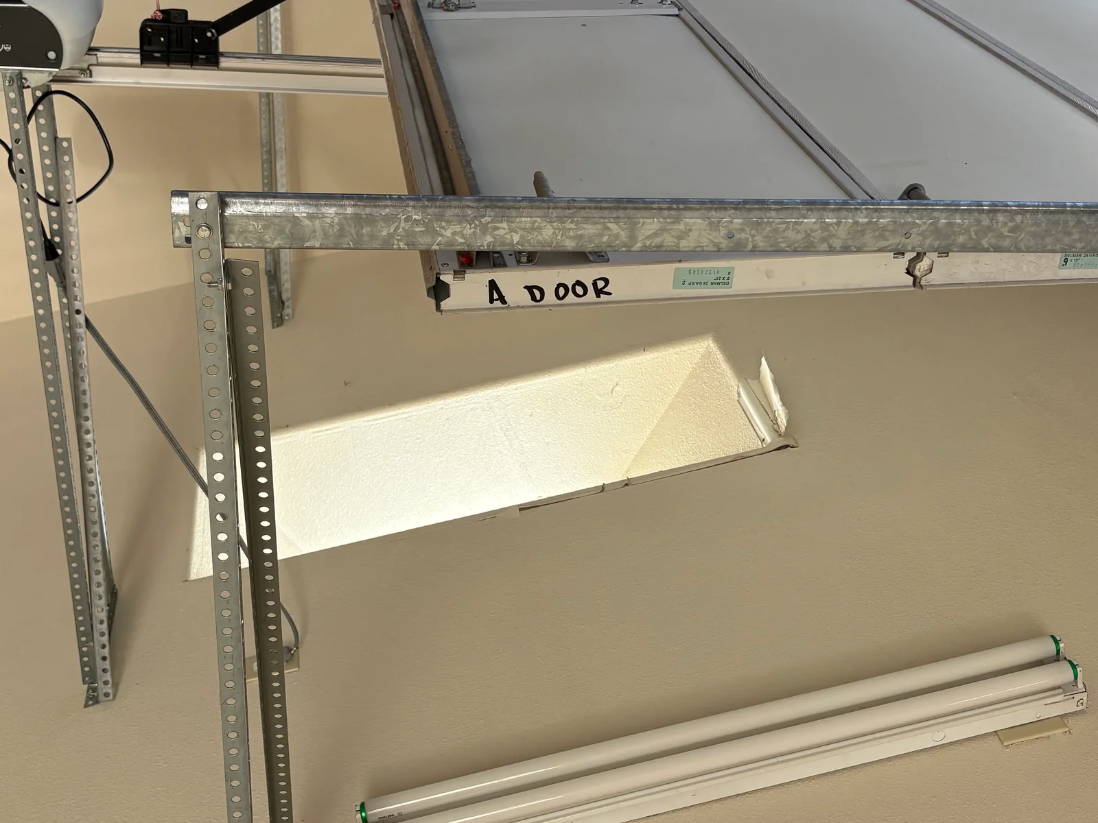Galvanized steel garage door track and perforated steel brackets with exposed white foam insulation and a ceiling-mounted opener