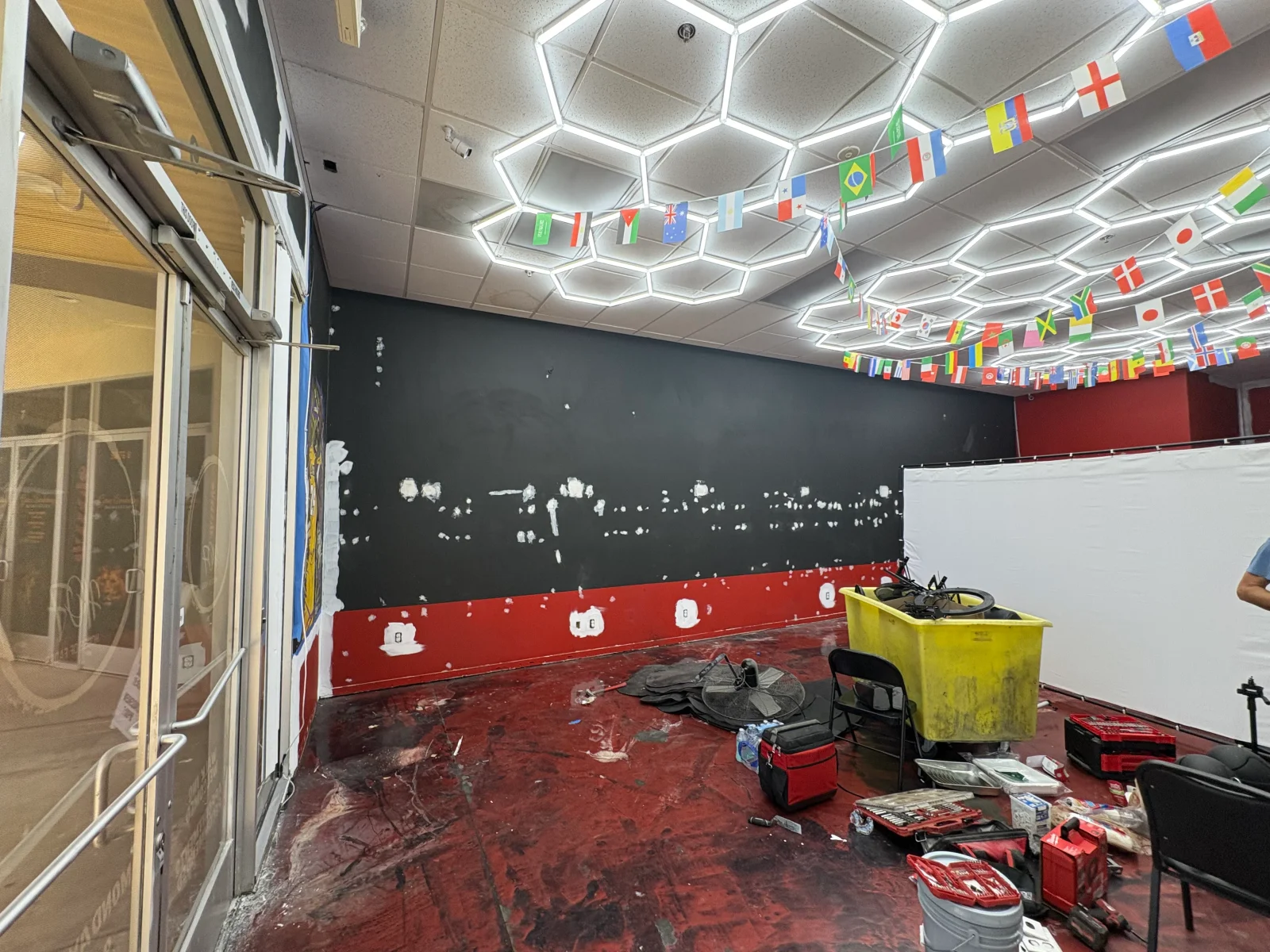 Charcoal commercial interior wall with white spackle patches, red lower band, and red coated floor with tools