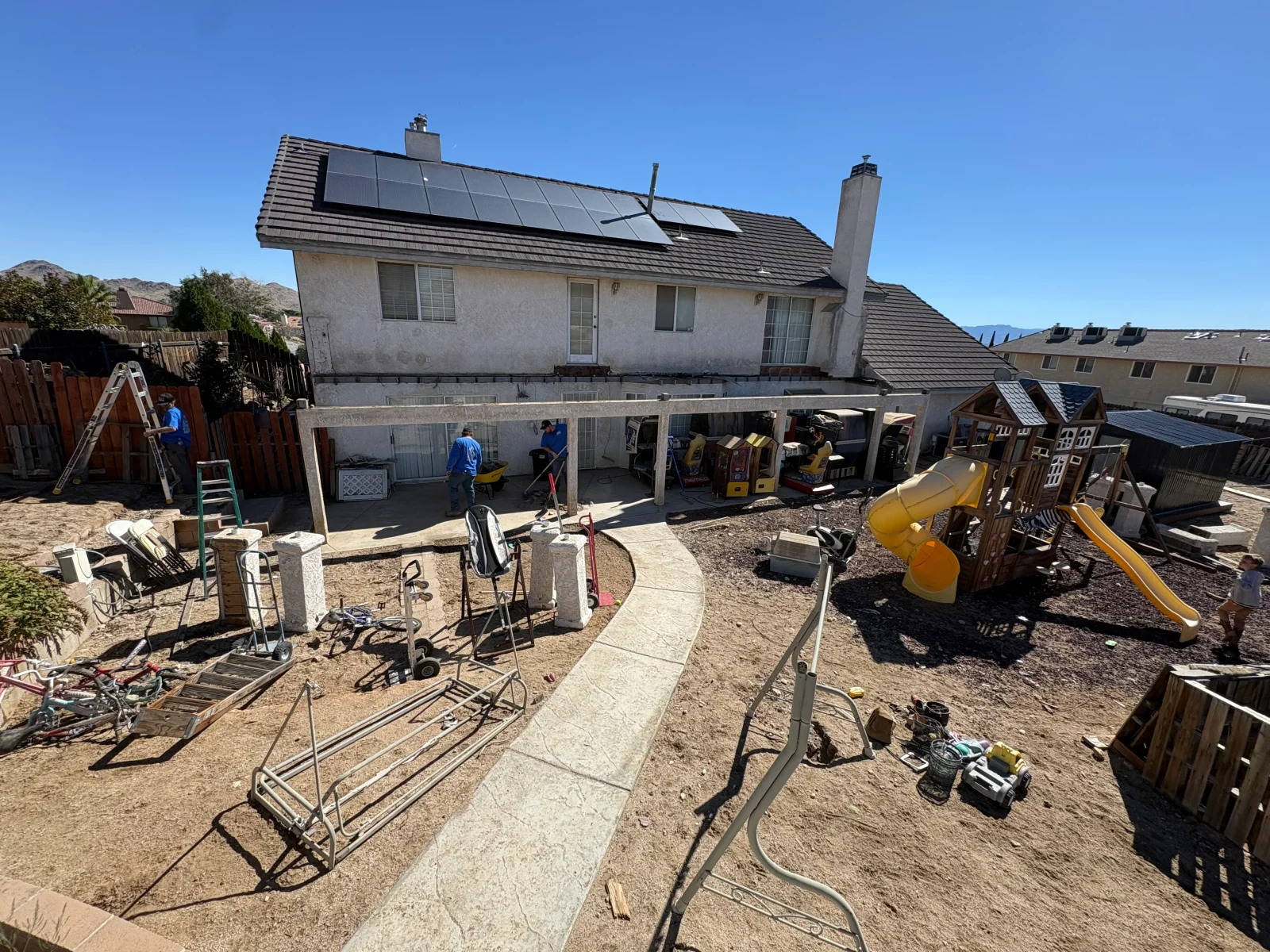 Backyard site with stamped concrete walkway, covered concrete patio beams, and debris clearing near a wood fence