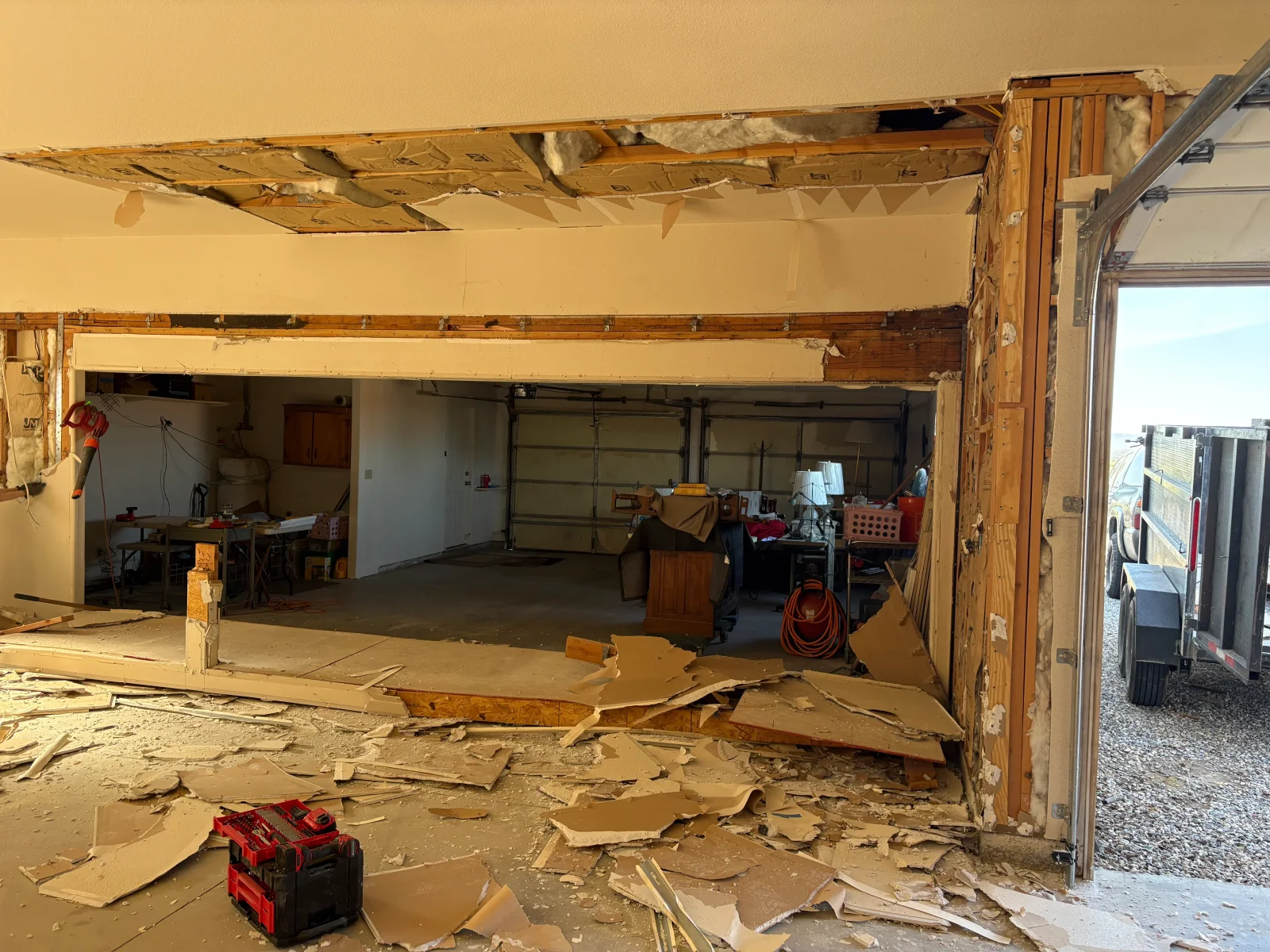 Demolished garage wall with exposed wood framing, removed drywall debris, and open ceiling insulation