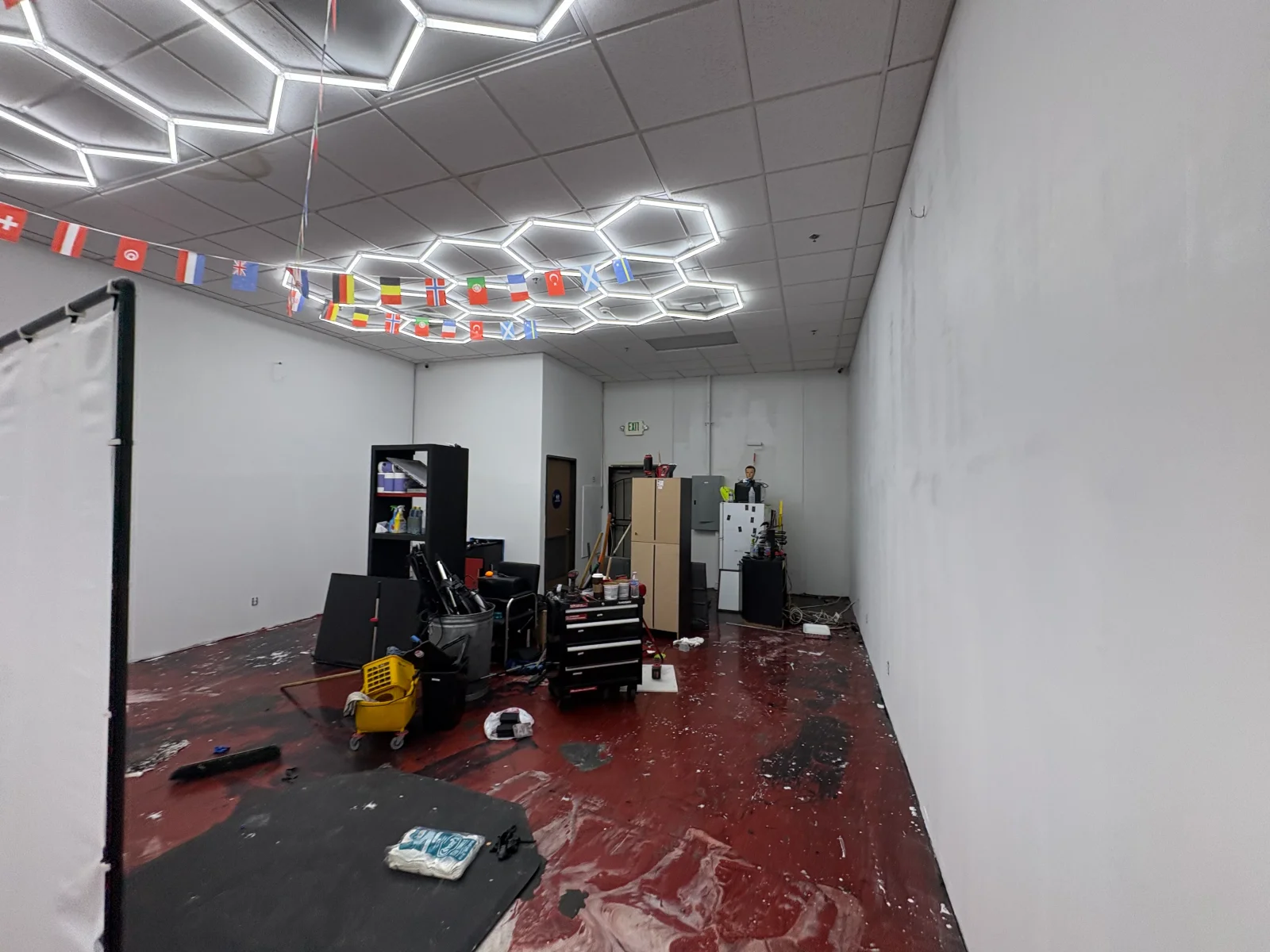 Commercial interior with red-brown coated concrete floor, white drywall, hexagonal LED ceiling lights, and staged tools