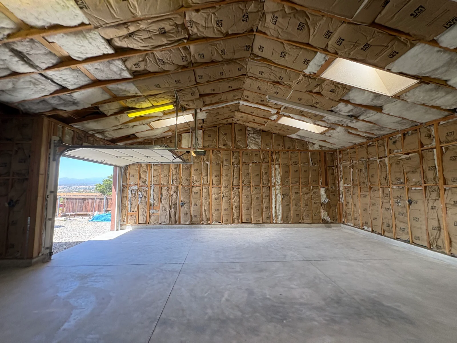 Garage interior with wood-framed walls and gabled ceiling filled with kraft-faced fiberglass batt insulation, skylights, and concrete floor