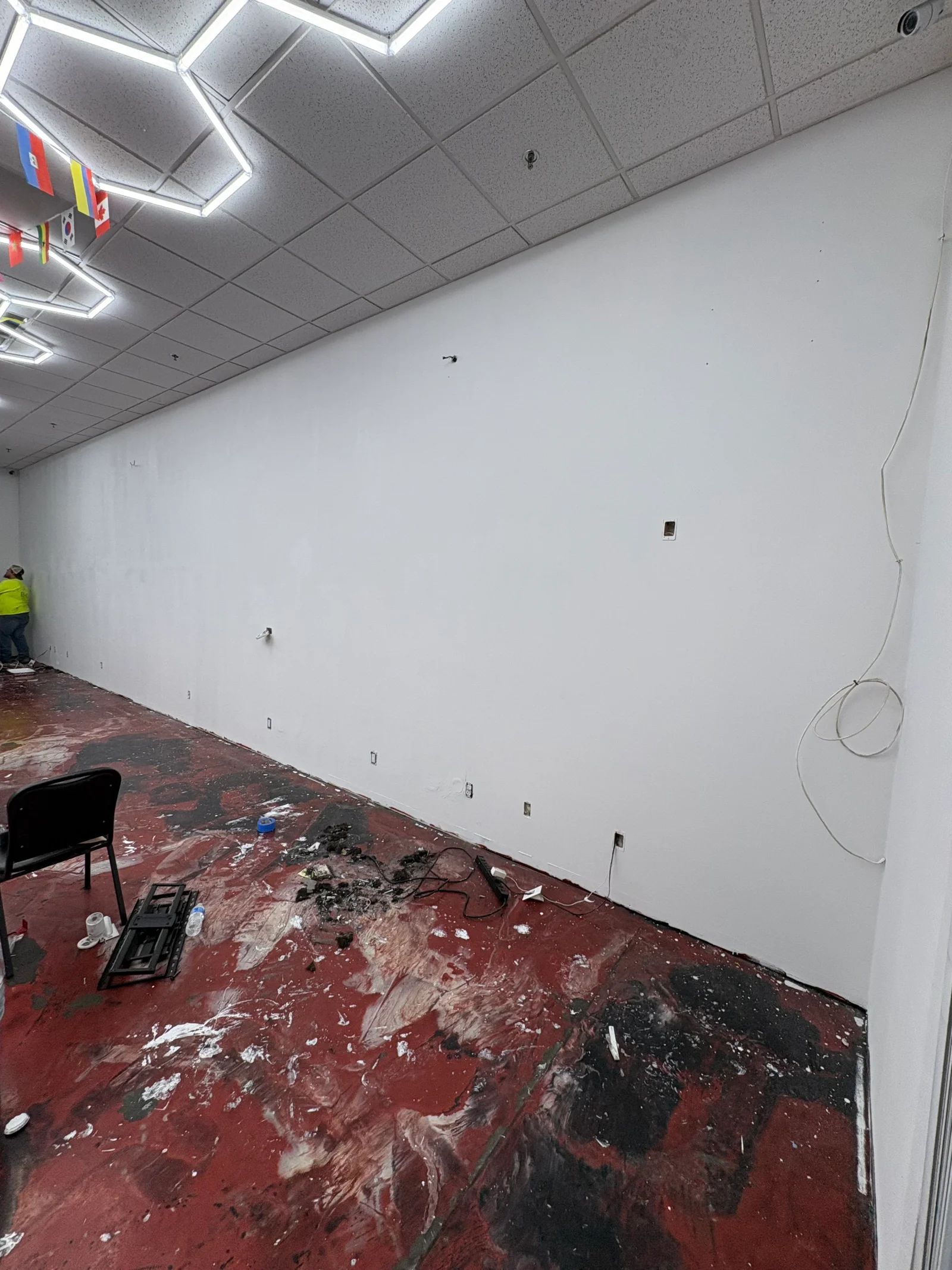 Large white interior wall with outlets and mounting holes above red concrete floor with paint debris and a wall bracket